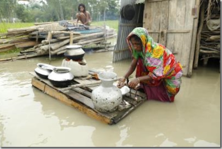 Una mujer cocina frente a su casa inundada en Mainkdir, Bogra, Bangladesh. Foto: Archivo EFE/Abir Abdullah.