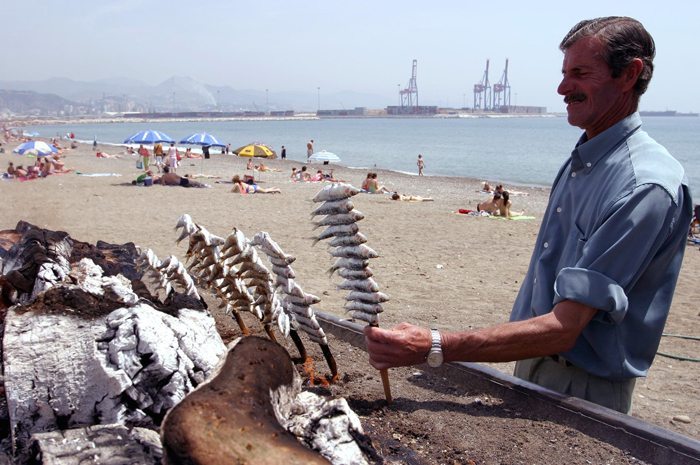 Un cocinero de un chiringuito hace espetos de sardinas en la playa de la barriada malagueñaa de Huelin.